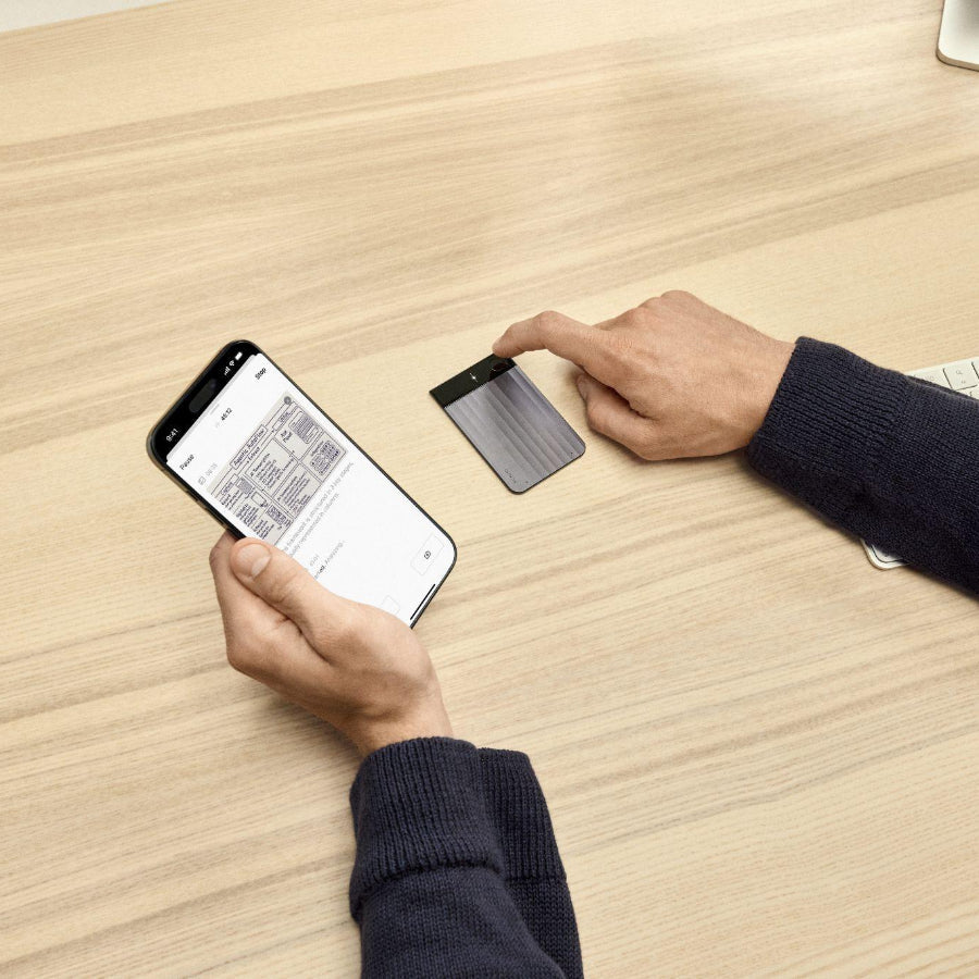 A person views meeting notes on the Plaud App while interacting with a gray Plaud Note Pro on a wooden desk.