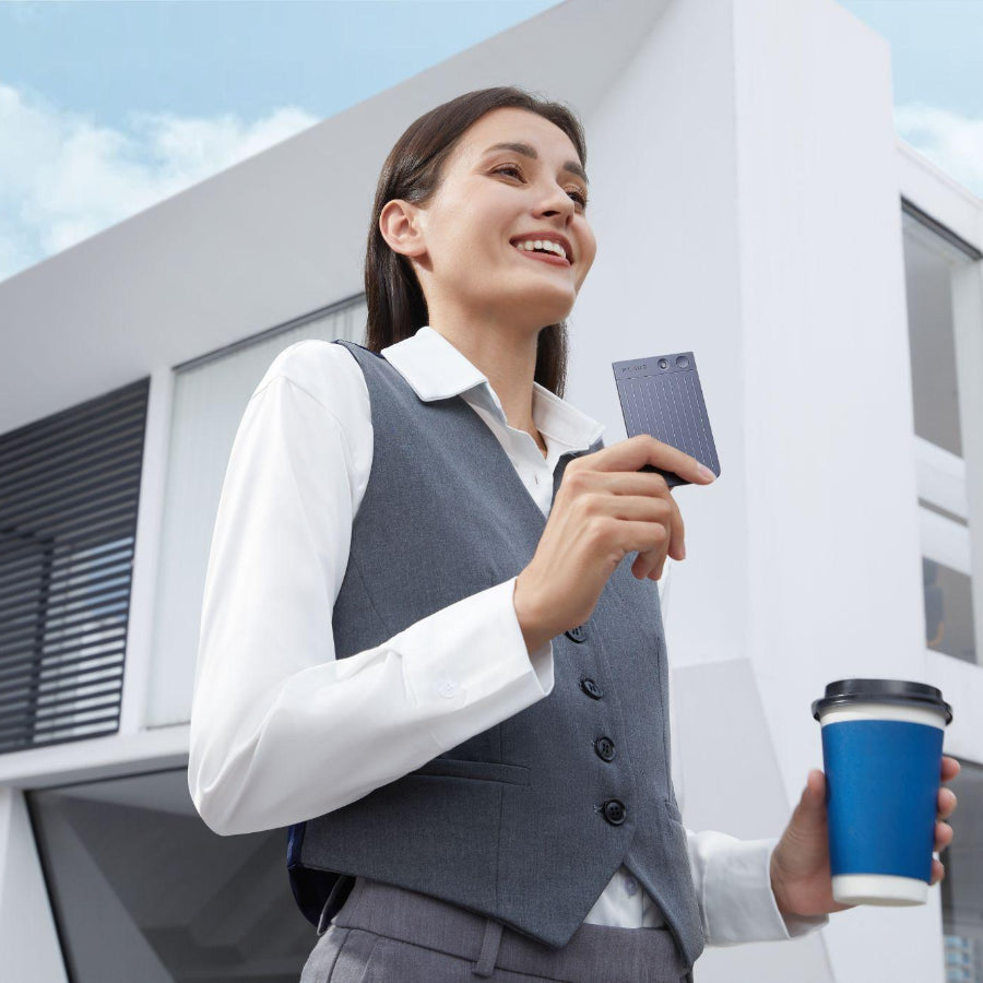 Woman in business attire holds a black Plaud Note and coffee outside a modern building.