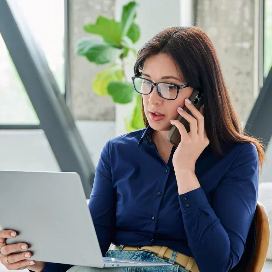 Woman on a phone call using a black Plaud Note attached to her smartphone while working on a laptop.