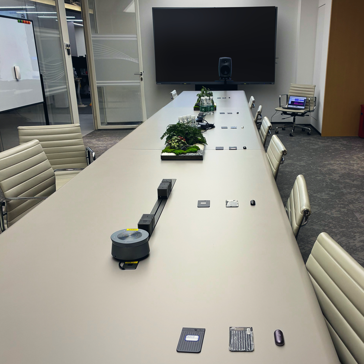 A sleek conference room with a long gray table, featuring several Plaud Note Pro and Plaud NotePin S AI voice recorders.