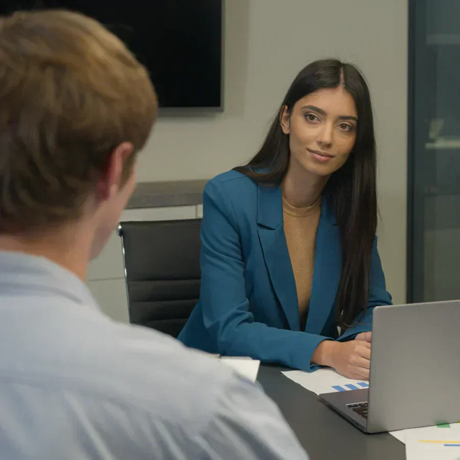 A professional woman wearing a Plaud NotePin on her teal blazer during an office meeting.