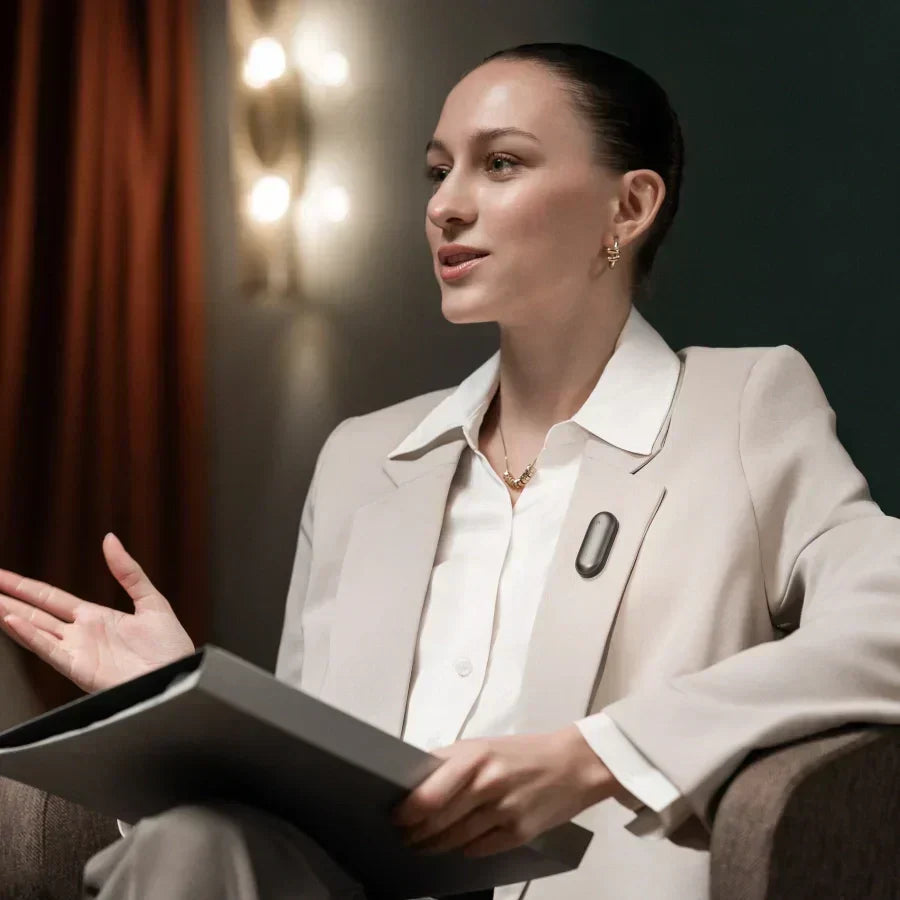 Professional woman wearing a Cosmic Gray Plaud NotePin on her blazer lapel while speaking.