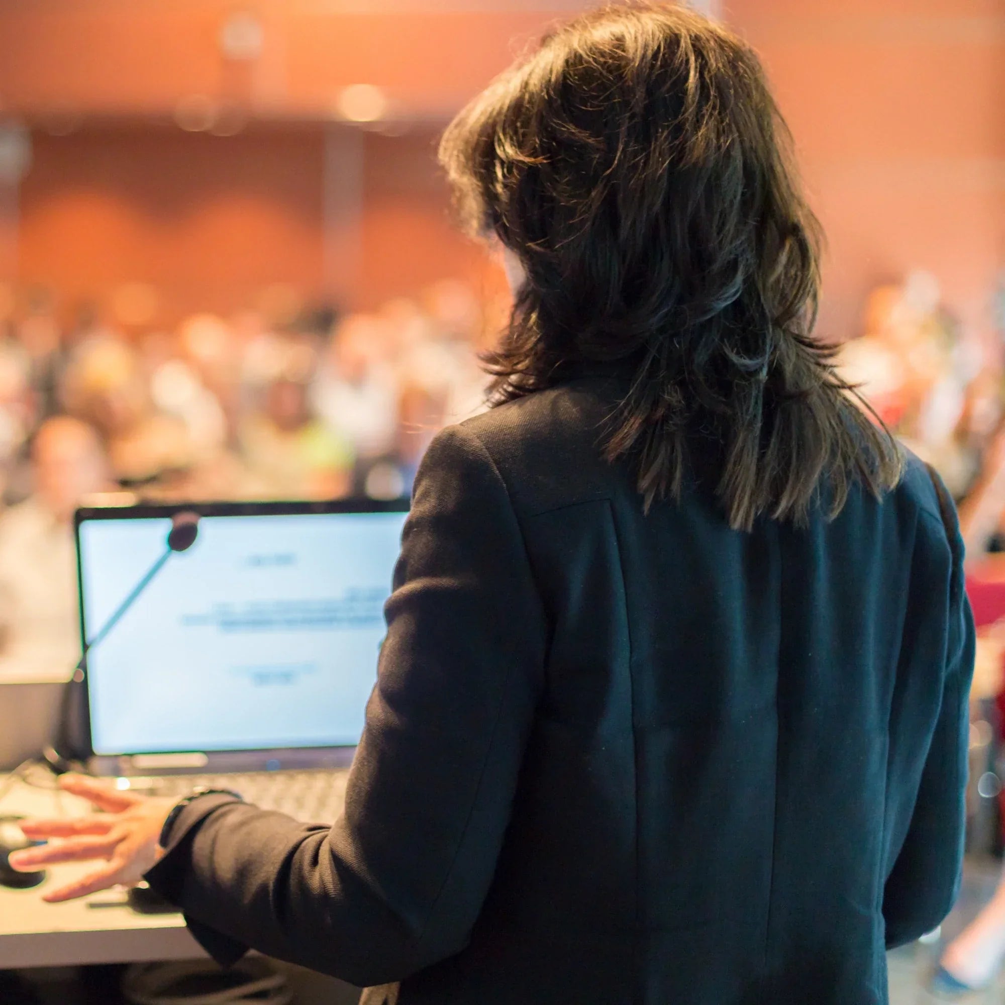 Lecturer presenting to a large audience in a lecture hall, seen from behind.
