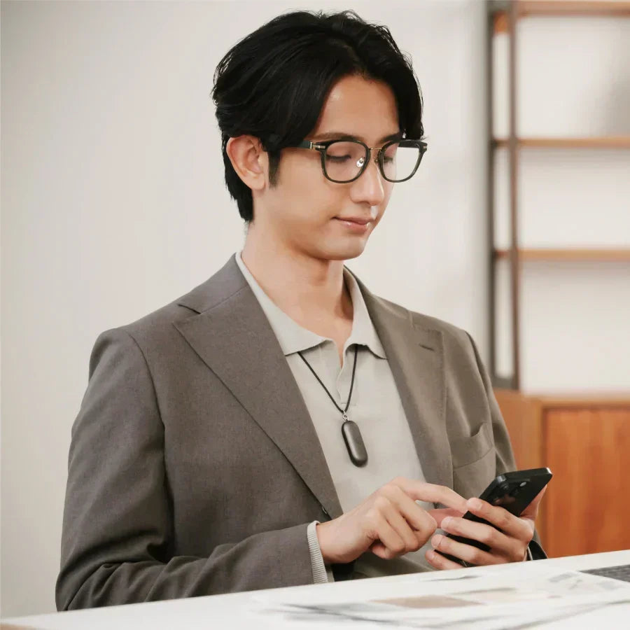 A man in a suit wearing a black Plaud NotePin on a lanyard while using his smartphone.