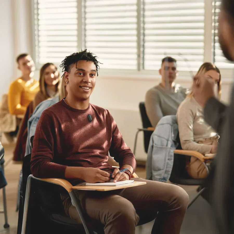 A student wearing a black Plaud NotePin on his sweater while listening in a classroom.