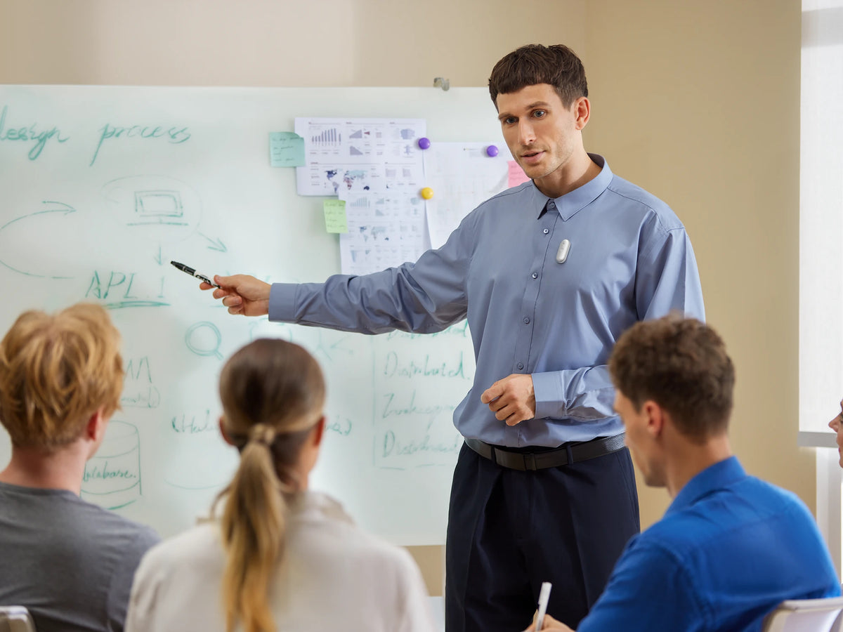 A man wearing a silver Plaud NotePin S on his shirt while presenting to a group at a whiteboard.