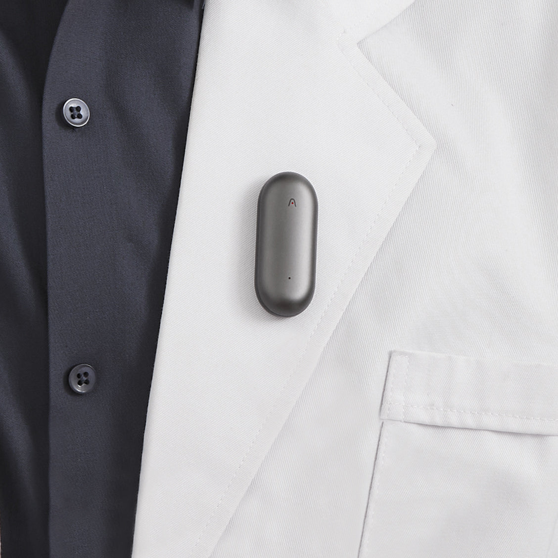 Plaud NotePin charcoal gray wearable voice recorder on white blazer, AI note taker, hands-free recording