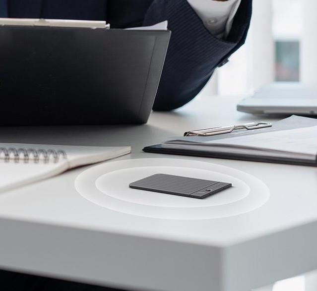 Black Plaud Note AI voice recorder on a white office desk, capturing audio in a professional meeting.