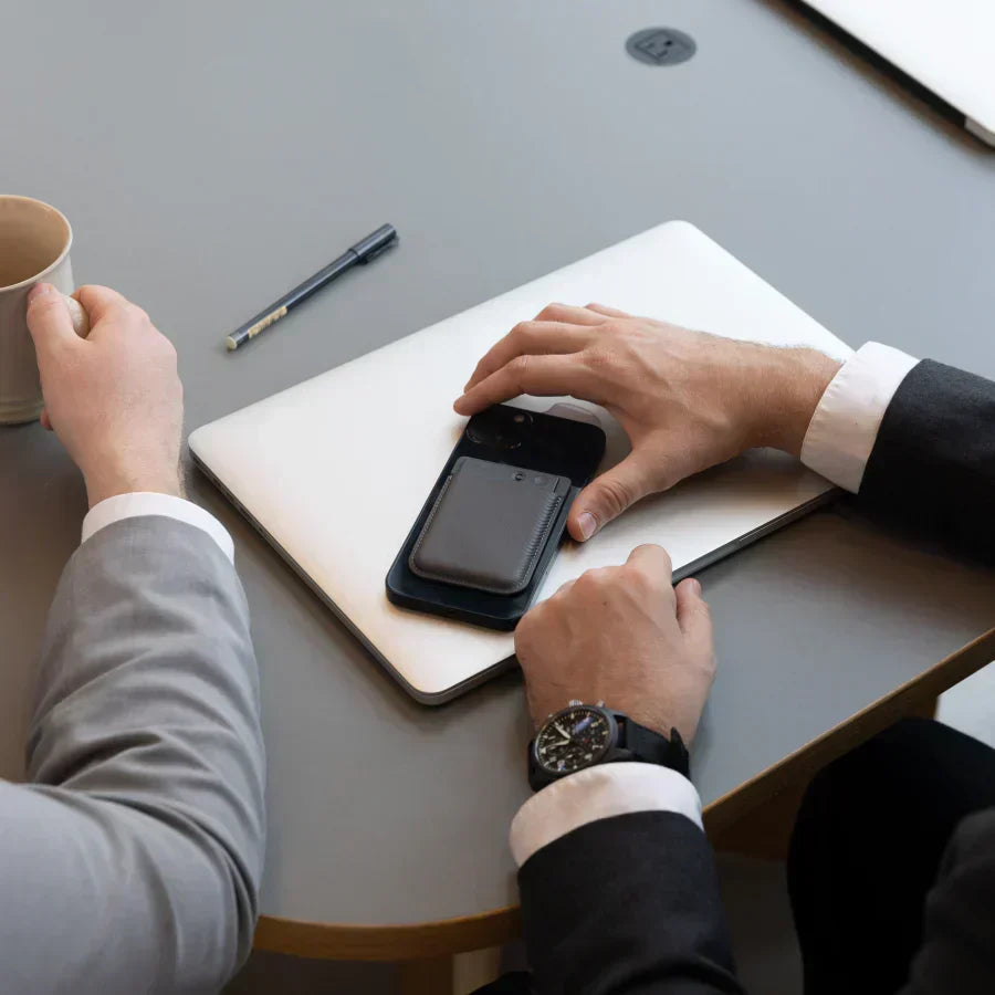 A black Plaud Note attached to a smartphone on a desk during a business meeting.