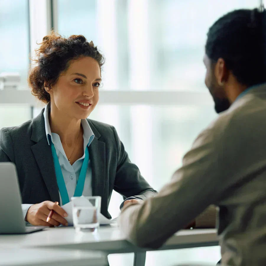 A woman wearing a silver Plaud NotePin on a lanyard during a professional meeting with a colleague.