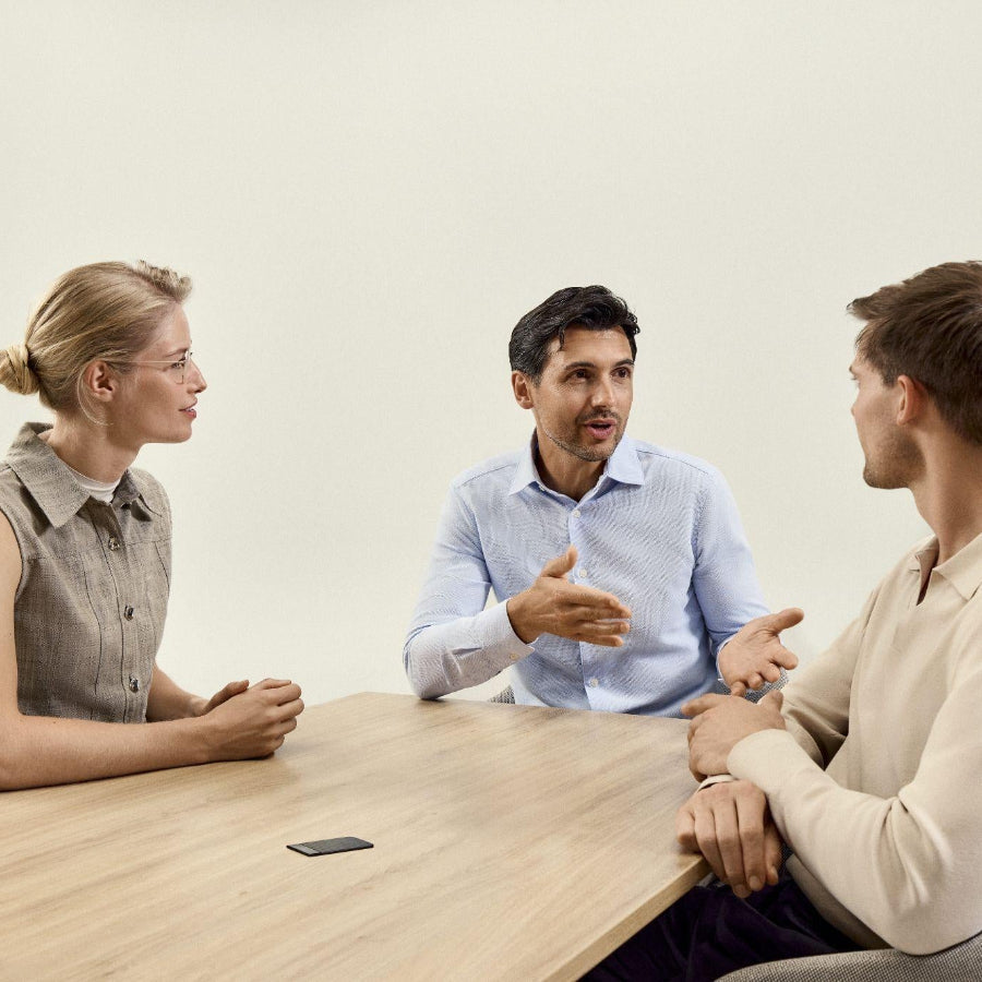 Three colleagues in a meeting with a black Plaud Note Pro recording on the table.