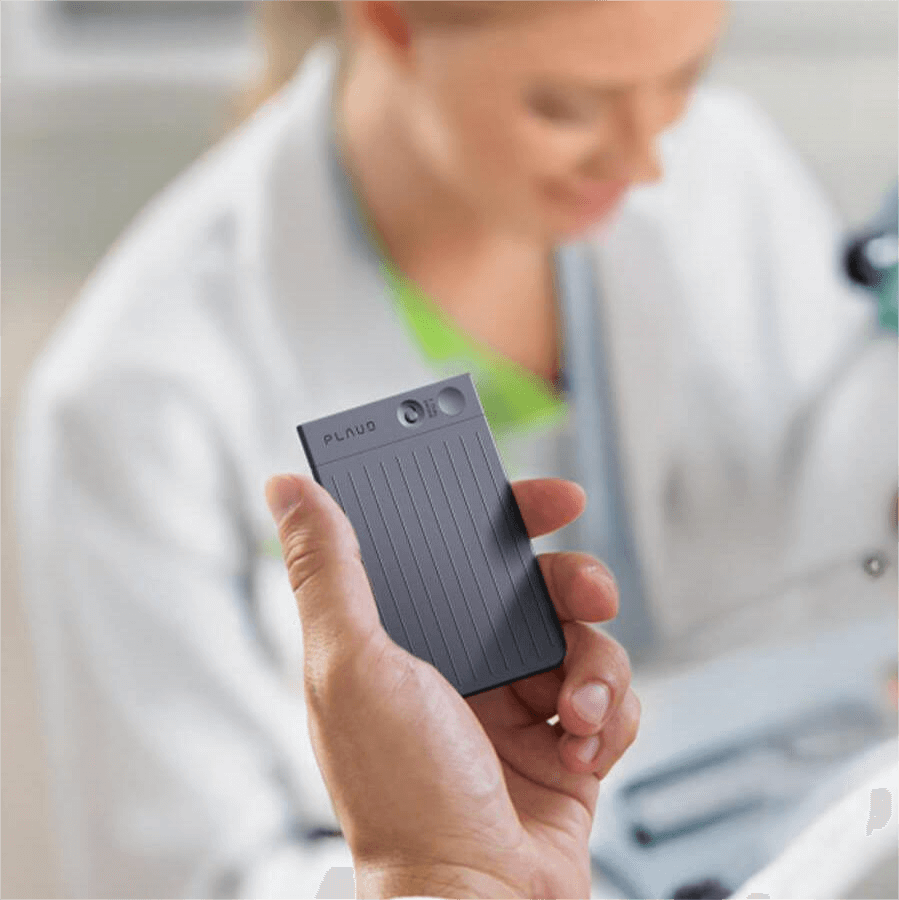 Hand holding Plaud Note device, with a doctor in the blurred background.