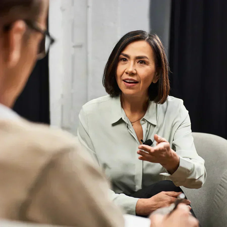 A woman wearing a black Plaud NotePin on her shirt while speaking during a meeting.