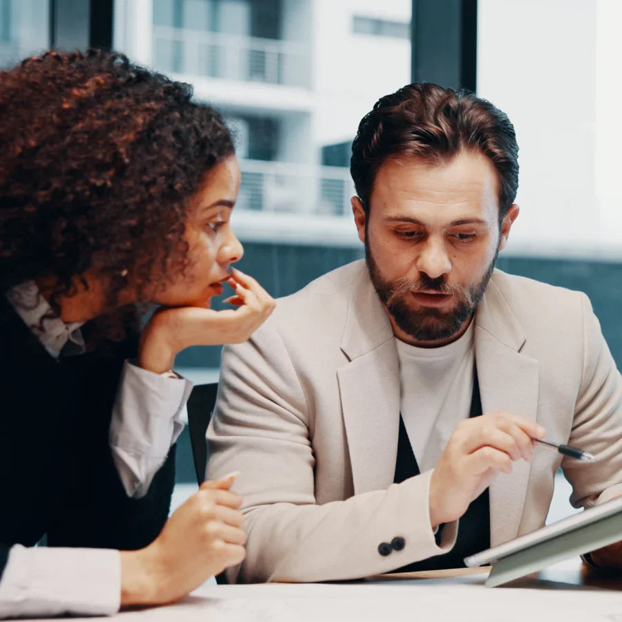 Man wearing a black Plaud NotePin on his lapel reviews a tablet with a colleague.