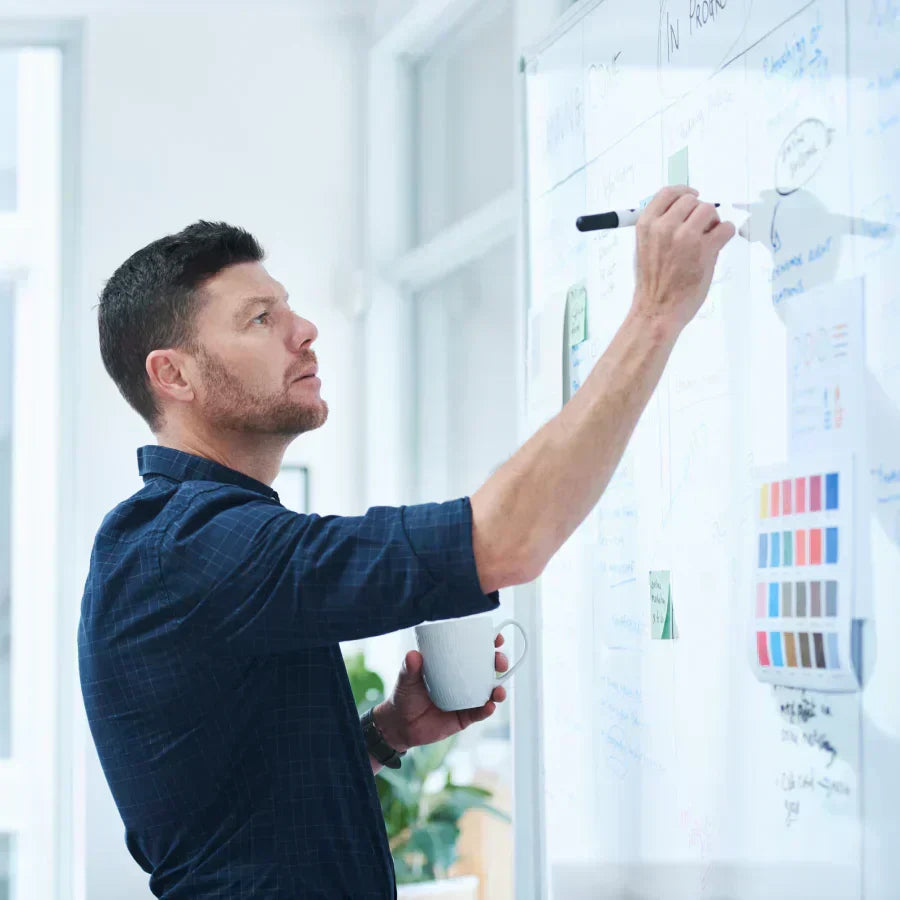 A man wearing a black Plaud NotePin on his wrist writes on a whiteboard during a brainstorming session.