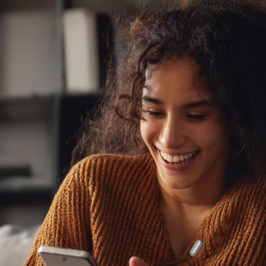 Smiling woman looking at her phone, with a small voice recorder device clipped to her top