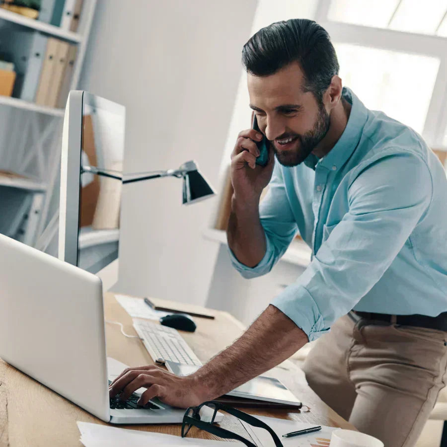 Professional using a black Plaud Note on his phone to record a call while working at a desk with a laptop.