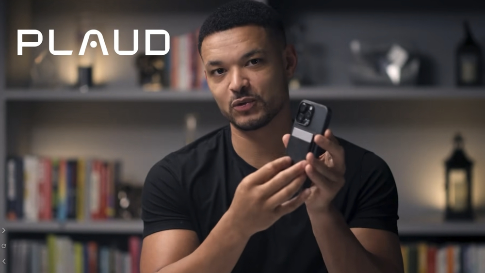 Steven Bartlett from The Diary Of A CEO using a black Plaud Note attached to the back of a smartphone.