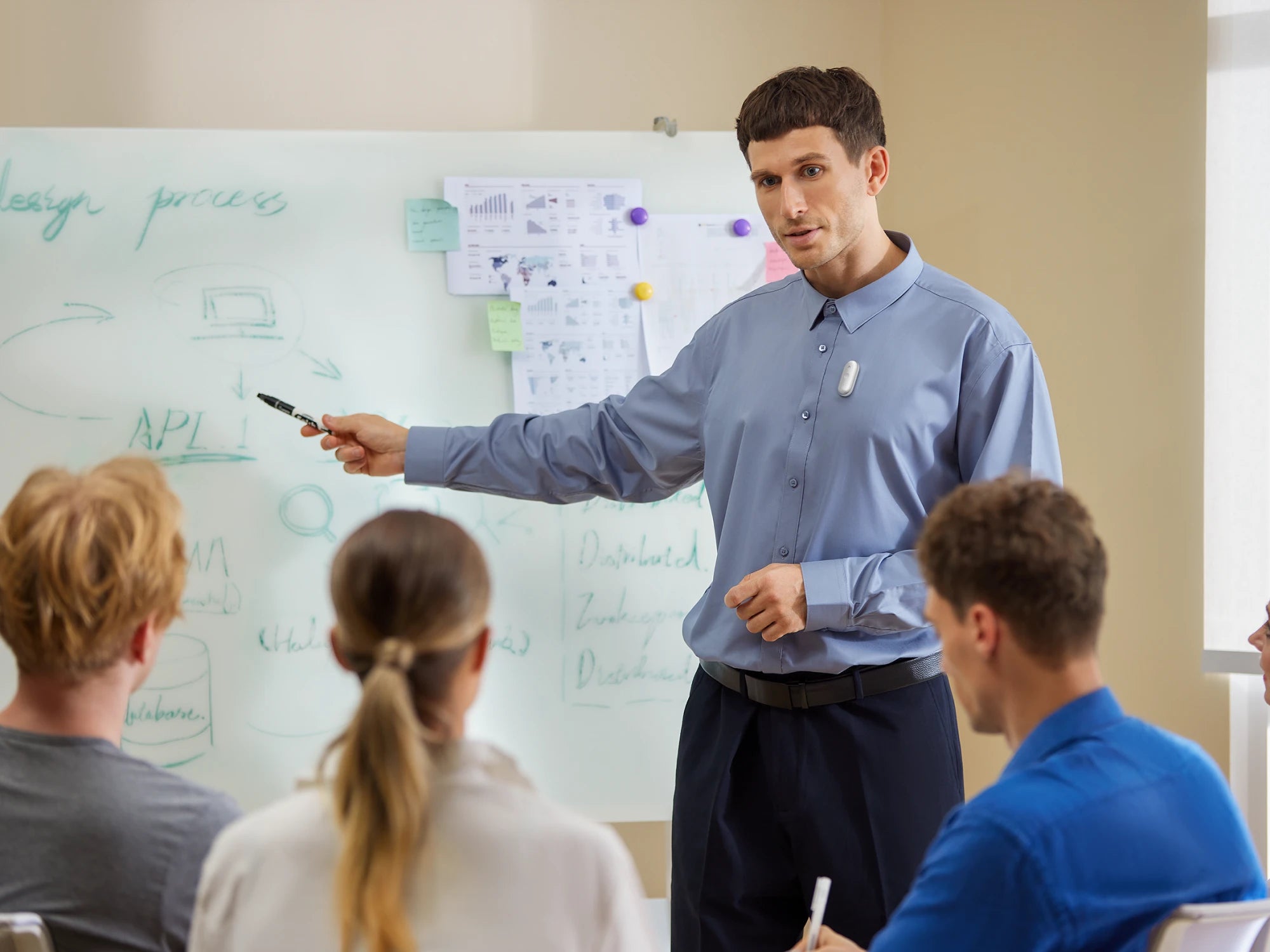 A man wearing a silver Plaud NotePin S on his shirt while presenting to a group at a whiteboard.
