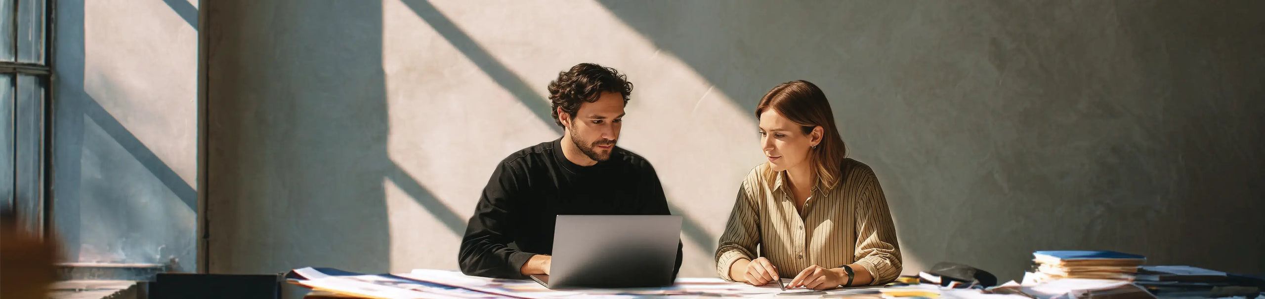 Two colleagues collaborating with Plaud AI note takers in a sunlit office.