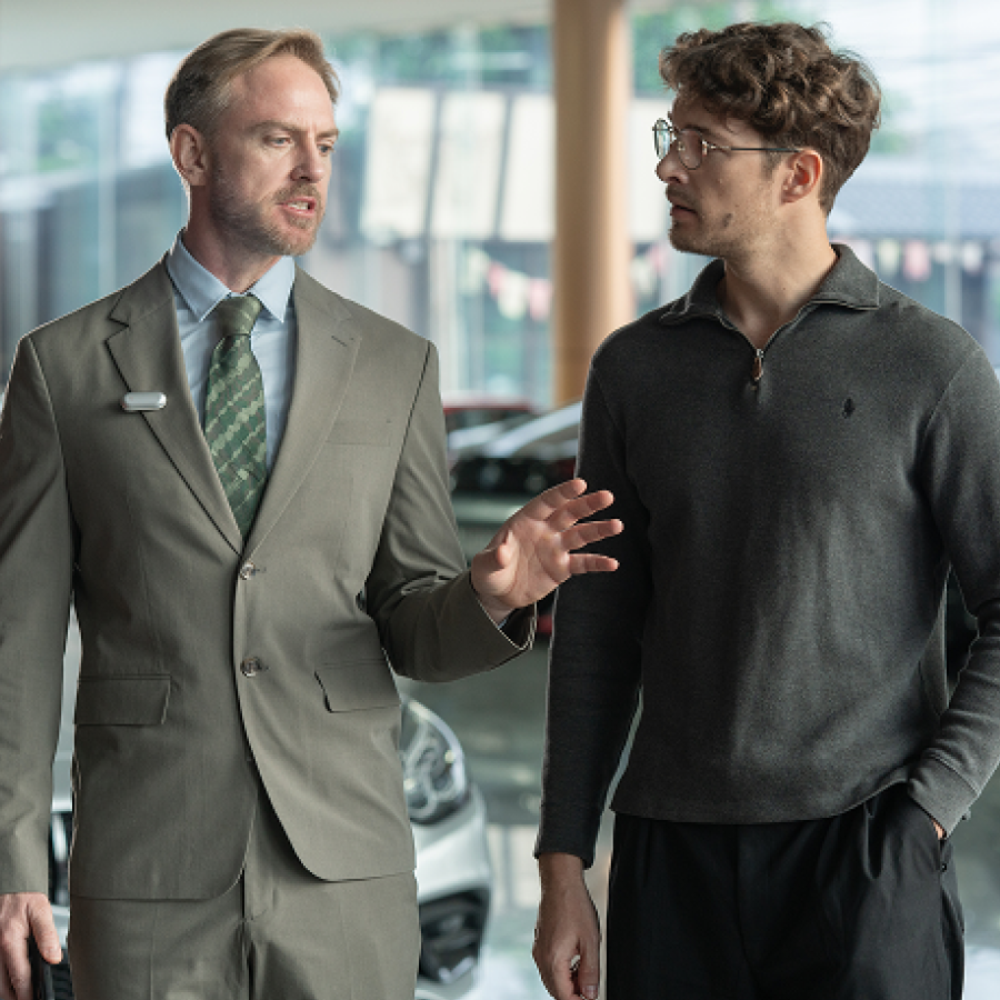 Professional in a suit wearing a silver Plaud NotePin while speaking with a client in a showroom.