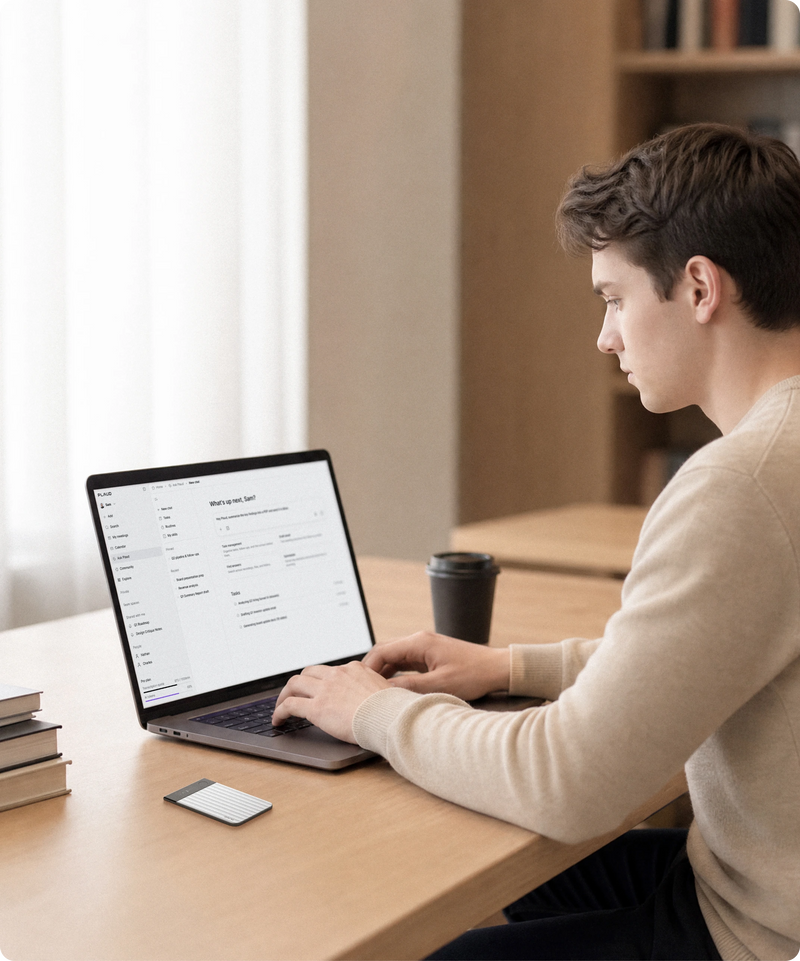 A student types on a laptop at a wooden table, with a silver Plaud Note Pro, a coffee cup, and books nearby.