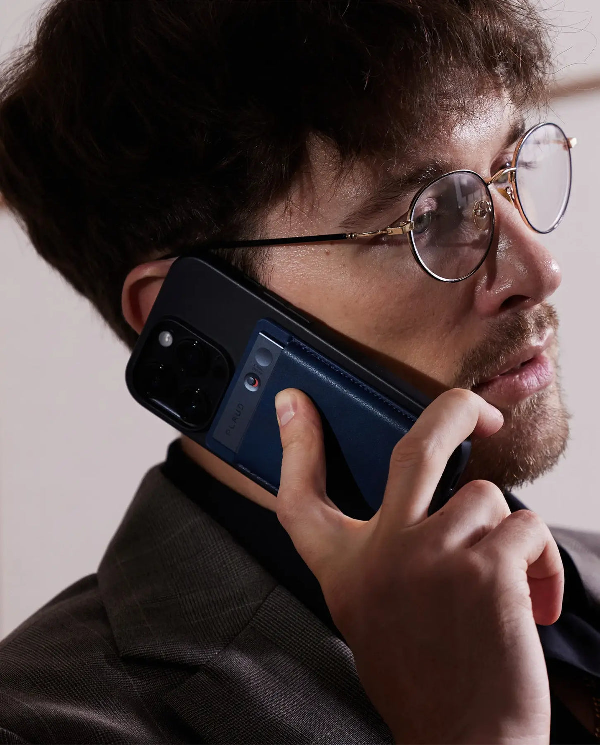 Man holding a phone with a Plaud Note attached to the back, pressing the button to record a call.
