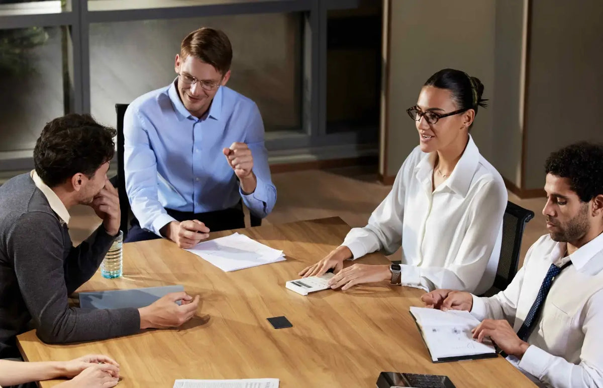 A team in a meeting with black and white Plaud Note devices on the table to record and transcribe the session.
