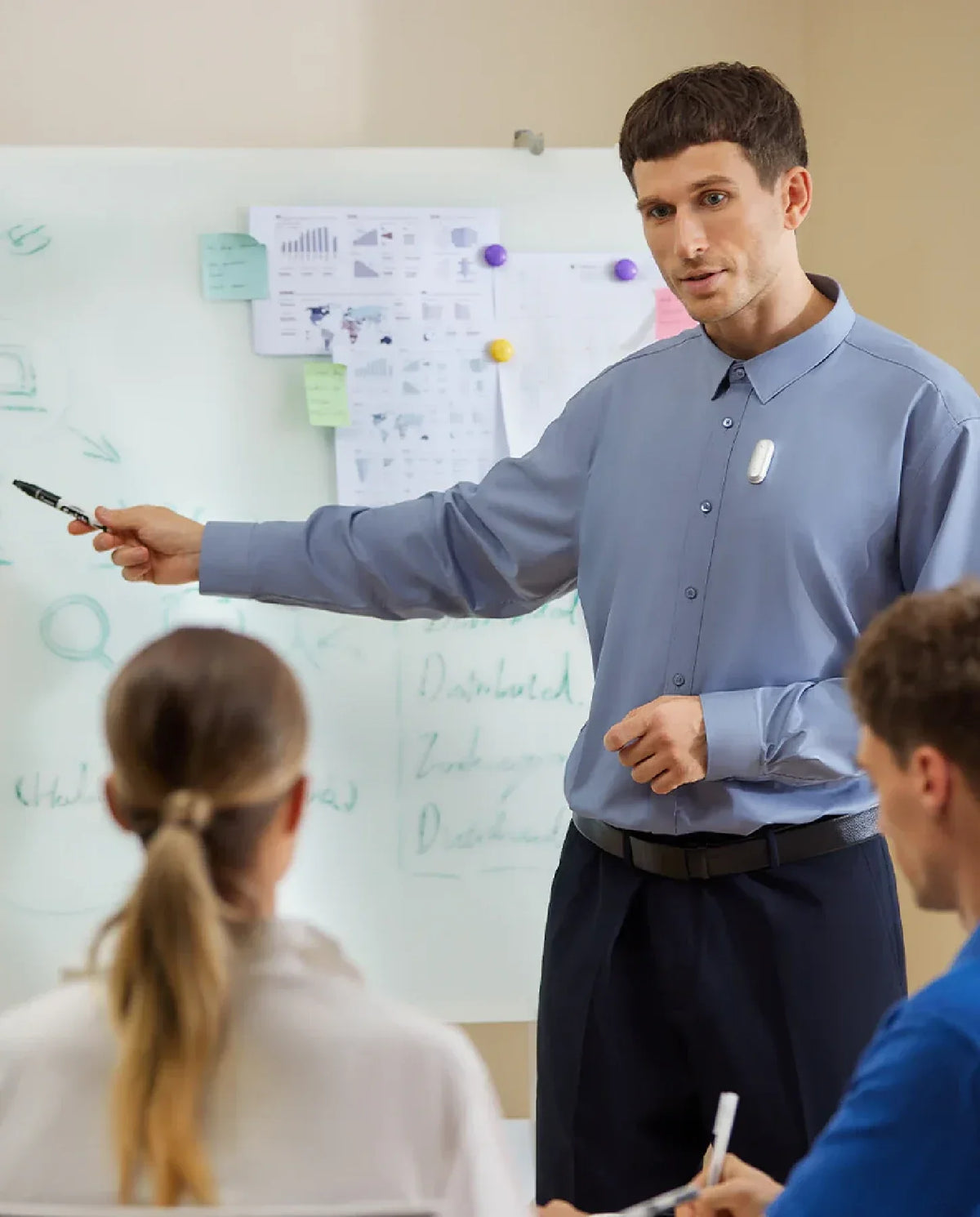 A man wearing a Plaud NotePin on his shirt while leading a presentation in an office setting.