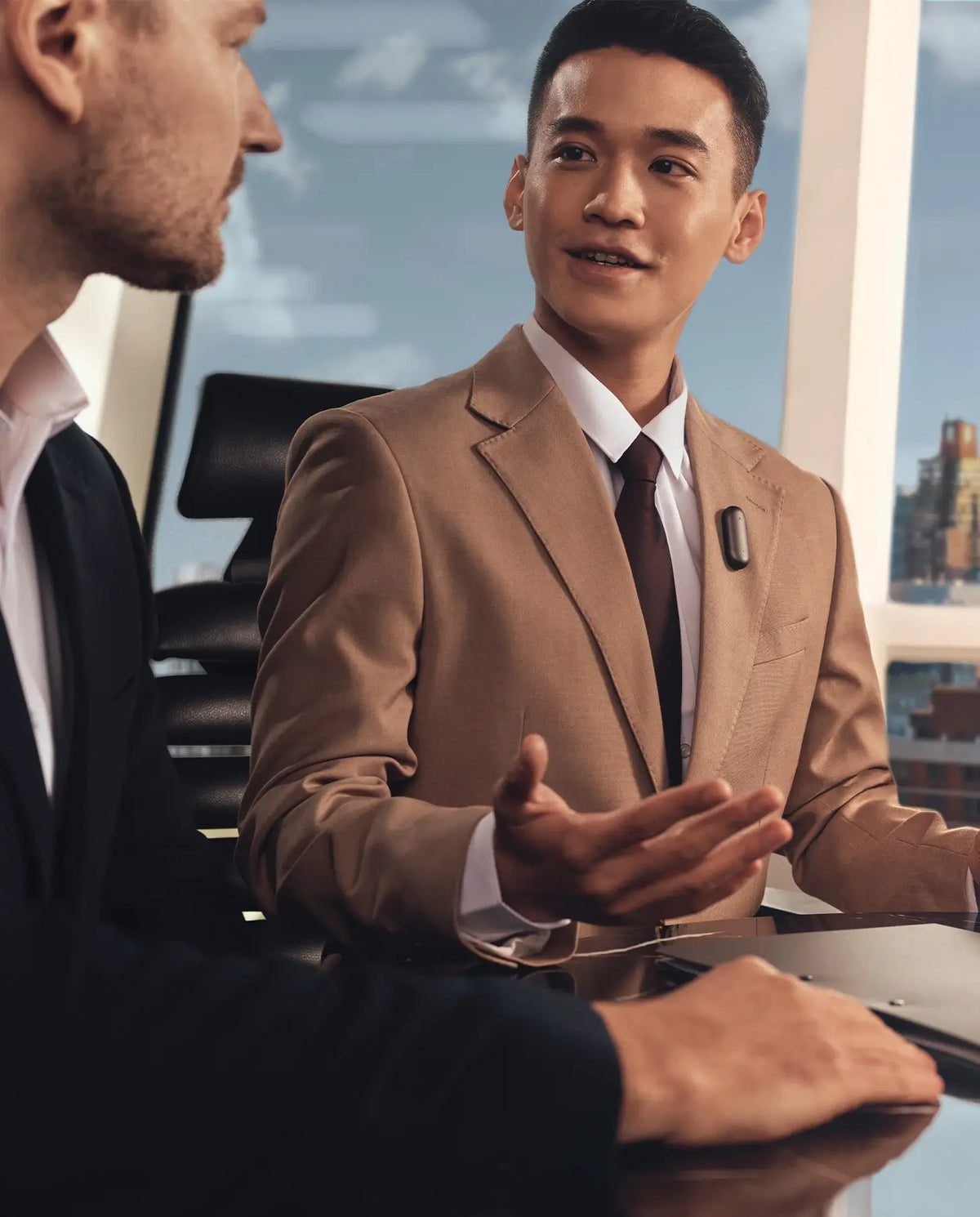 Professional in a tan suit wearing a Plaud NotePin on his lapel during a meeting.