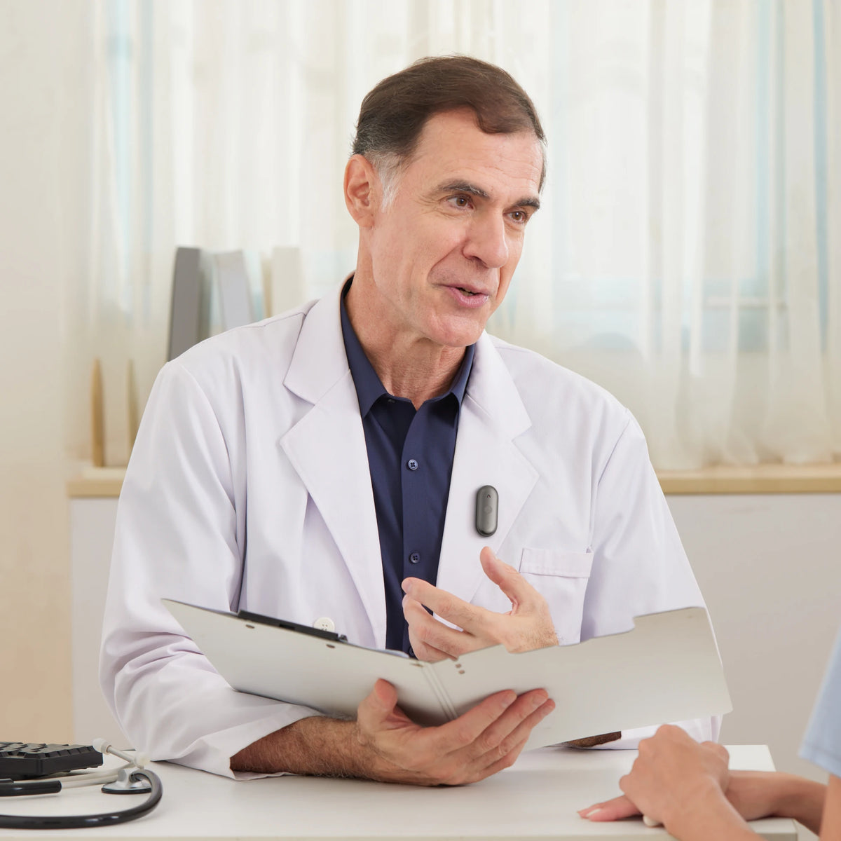 A doctor in a white coat wearing a Black Plaud NotePin S while consulting with a patient.
