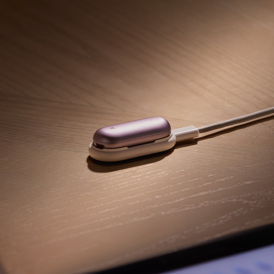 Lavender Plaud NotePin wearable AI note-taking device in white charging cradle on wooden surface, hands-free voice recorder for meetings and calls