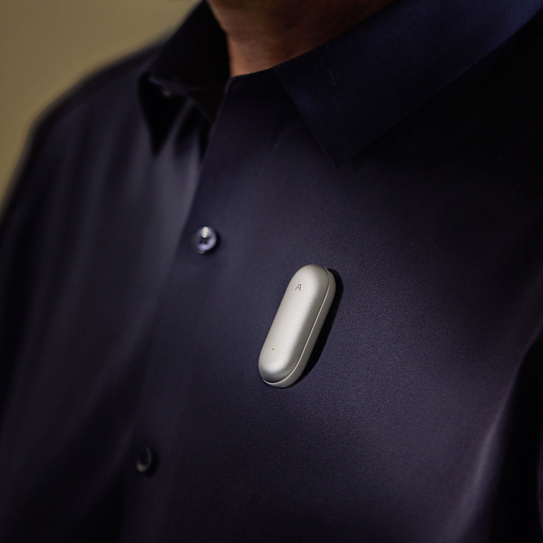 Sleek silver Plaud NotePin wearable AI voice recorder clipped to navy shirt demonstrating hands-free recording for meetings and interviews